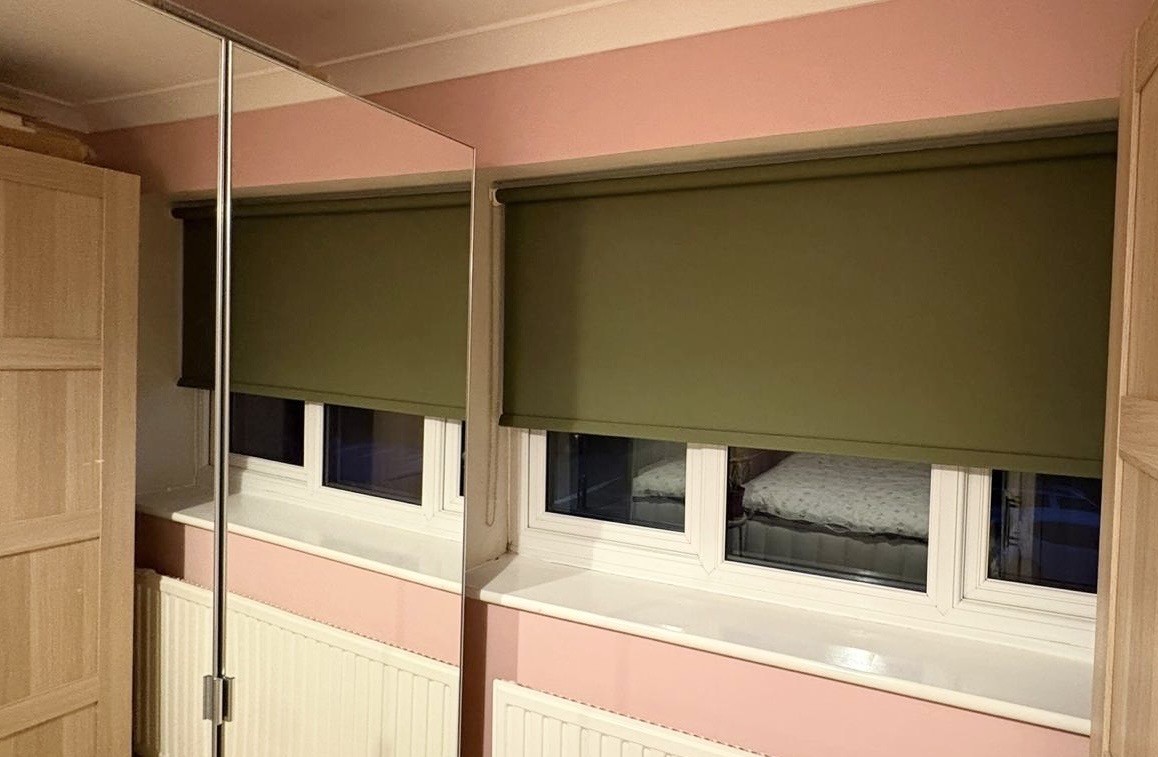 Green roller blind fitted in a pink bedroom