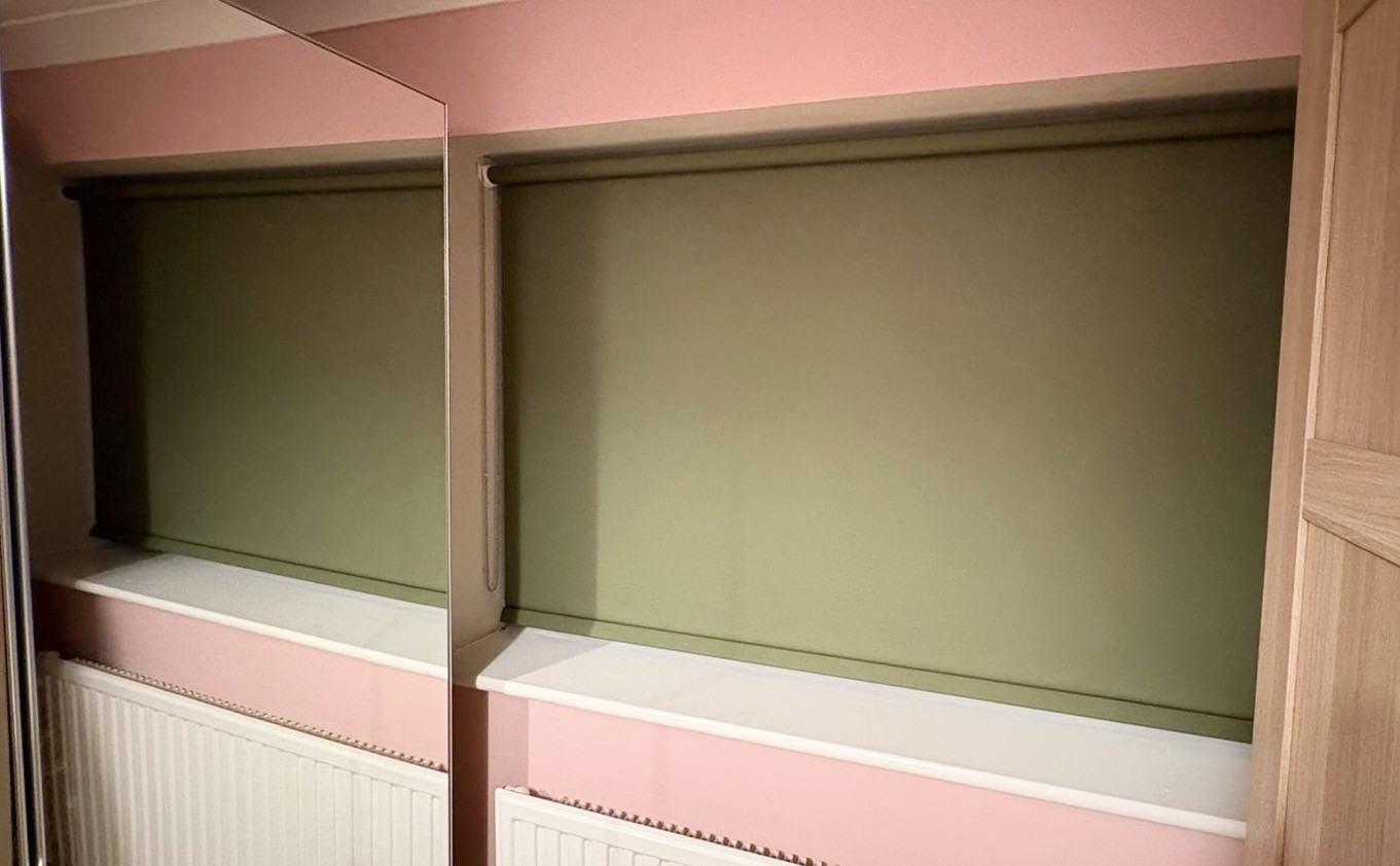 Green roller blind installed in a pink room