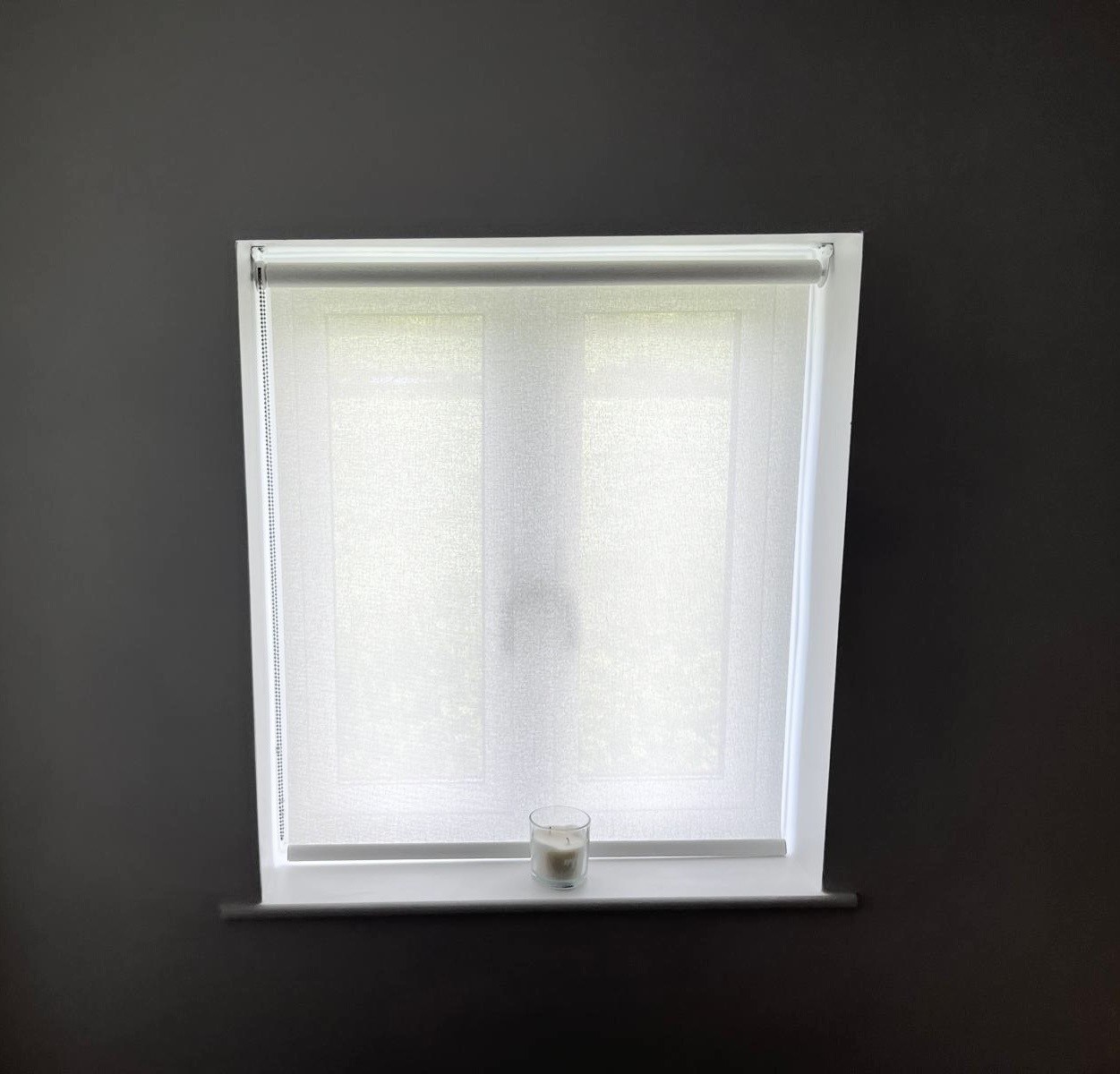 Closed white roller blind installed in a grey room.